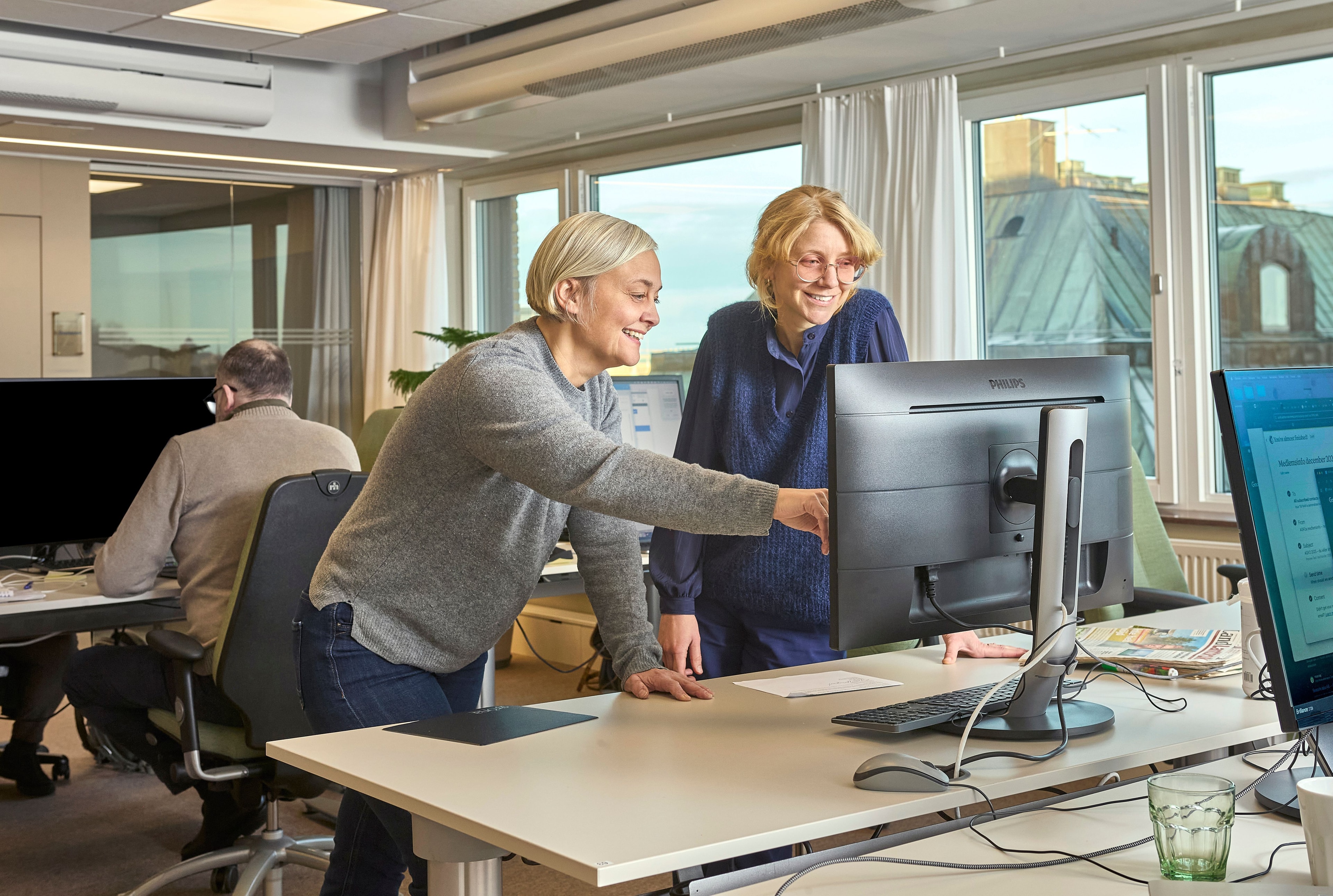 Två personer från Land Lantbruks redaktion som tittar på en skärm och har roligt tillsammans. 